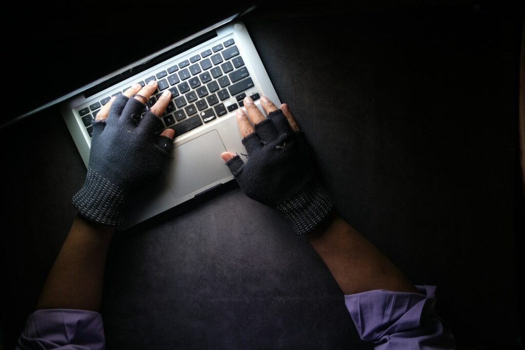 A hacker’s gloved hands typing on a laptop keyboard.
