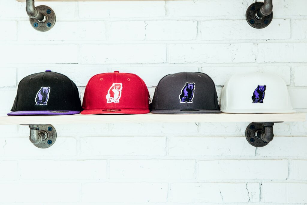 A set of four baseball caps on a shelf in the colors of black, gray, red, and white.