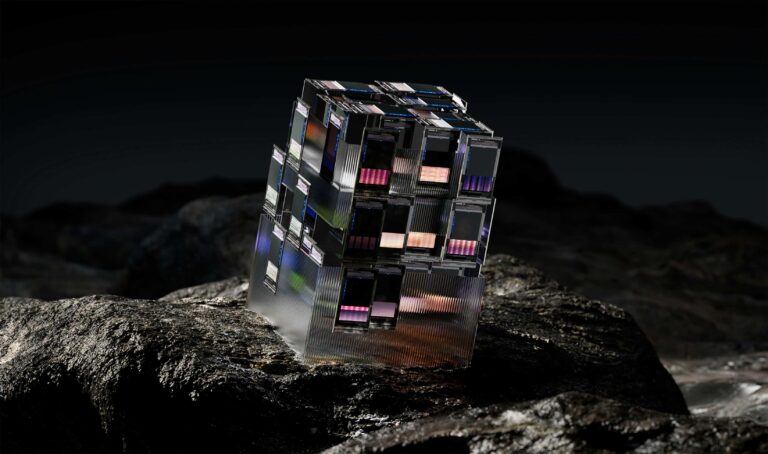 An abstract, metallic cube with digital screens sits on a dark, rocky landscape.