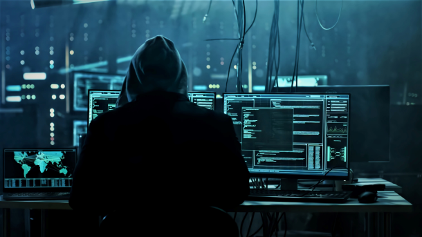 A hooded cybercriminal at his desk