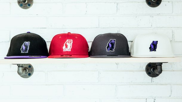 A set of four baseball caps on a shelf in the colors of black, gray, red, and white.